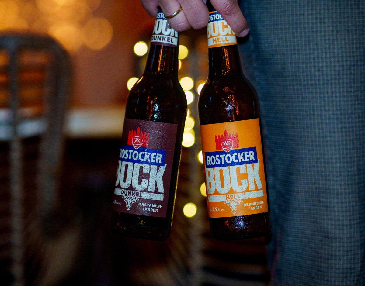 Nahaufnahme einer Hand mit 2 Flaschen Rostocker Bockbier, im Hintergrund Tisch und Stuhl.