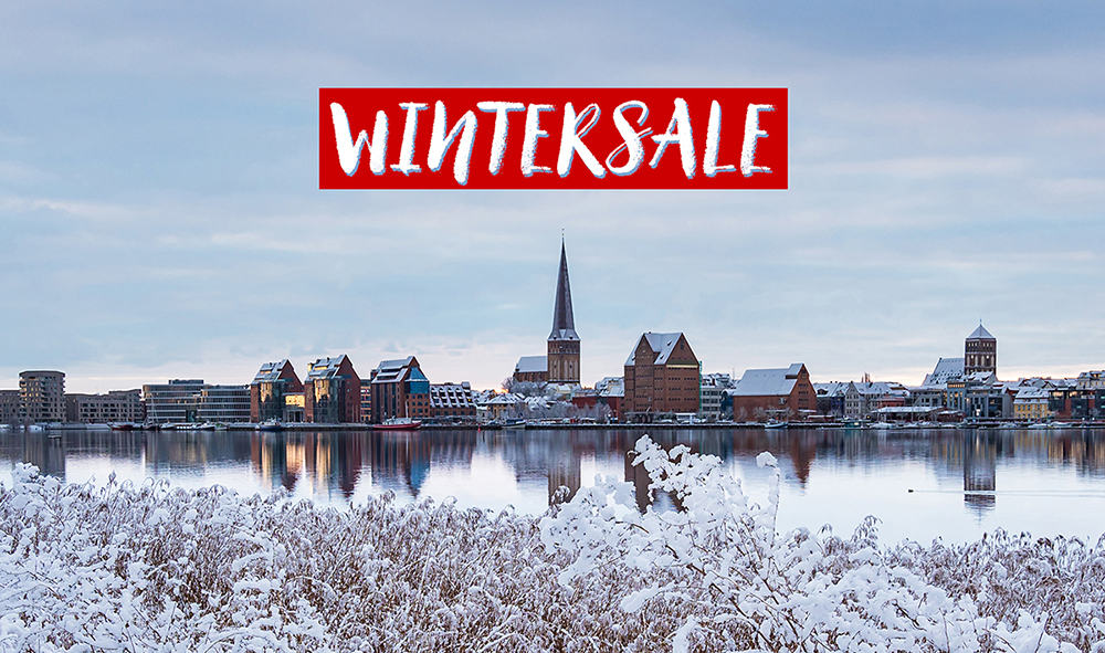 Ein verschneiter Stadtblick mit Gebäuden am Ufer eines Gewässers im Hintergrund und einer roten Schrift auf weißem Grund die Wintersale bedeutet.