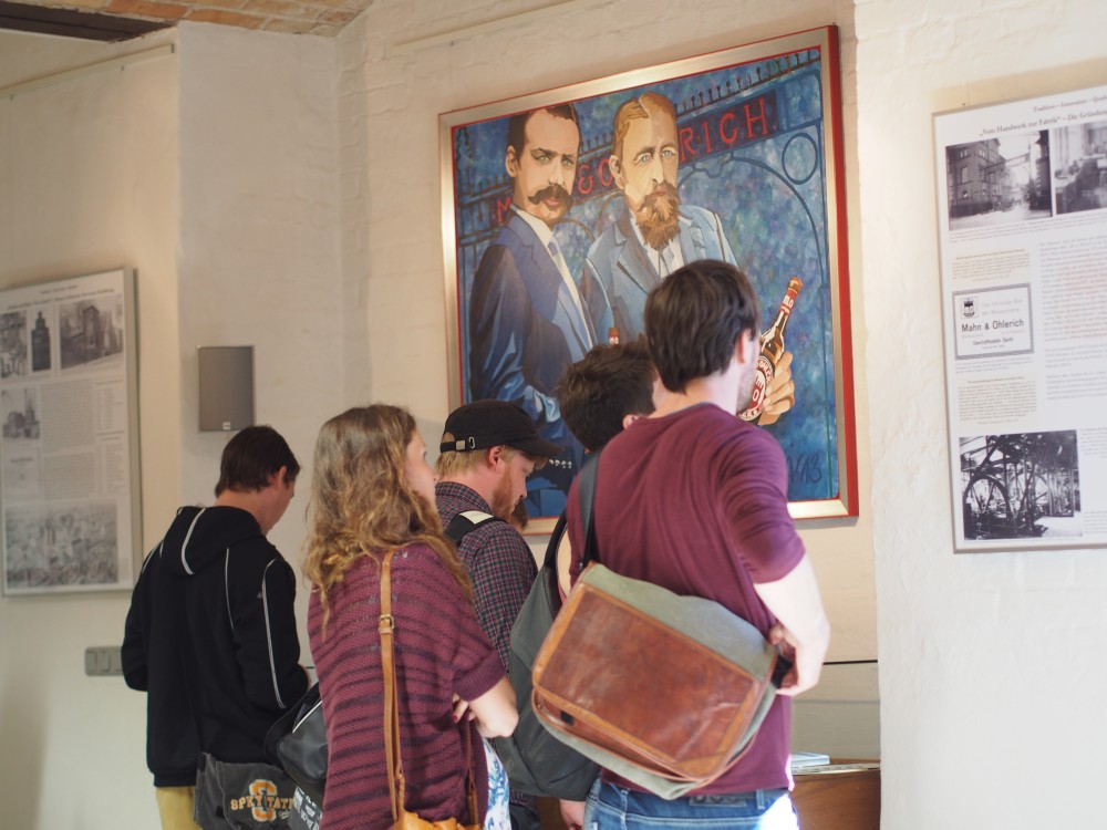 Mehrere Personen betrachten ein großes Porträt von zwei Männern in einem Museum.