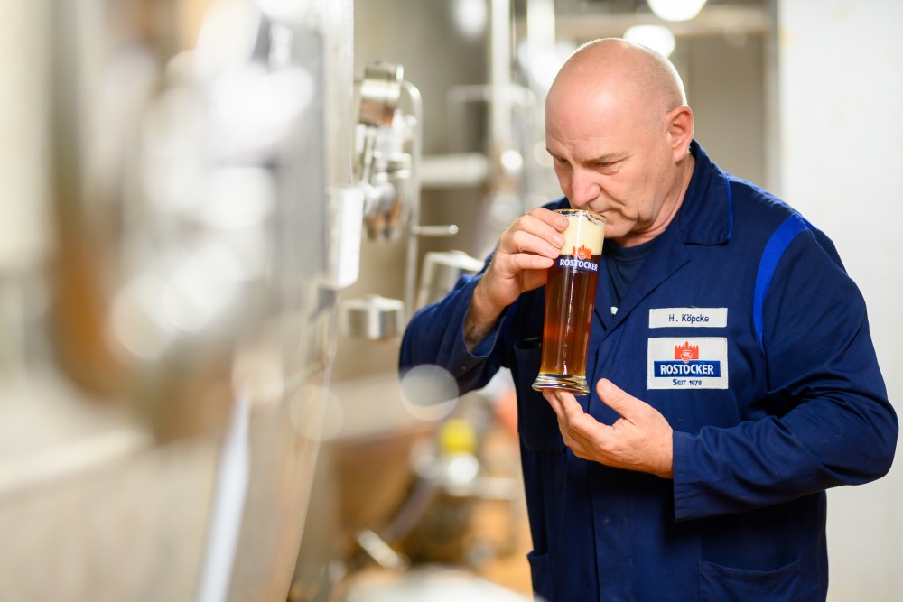 Ein Mann in Arbeitskleidung trinkt genüsslich aus einem Bierglas.