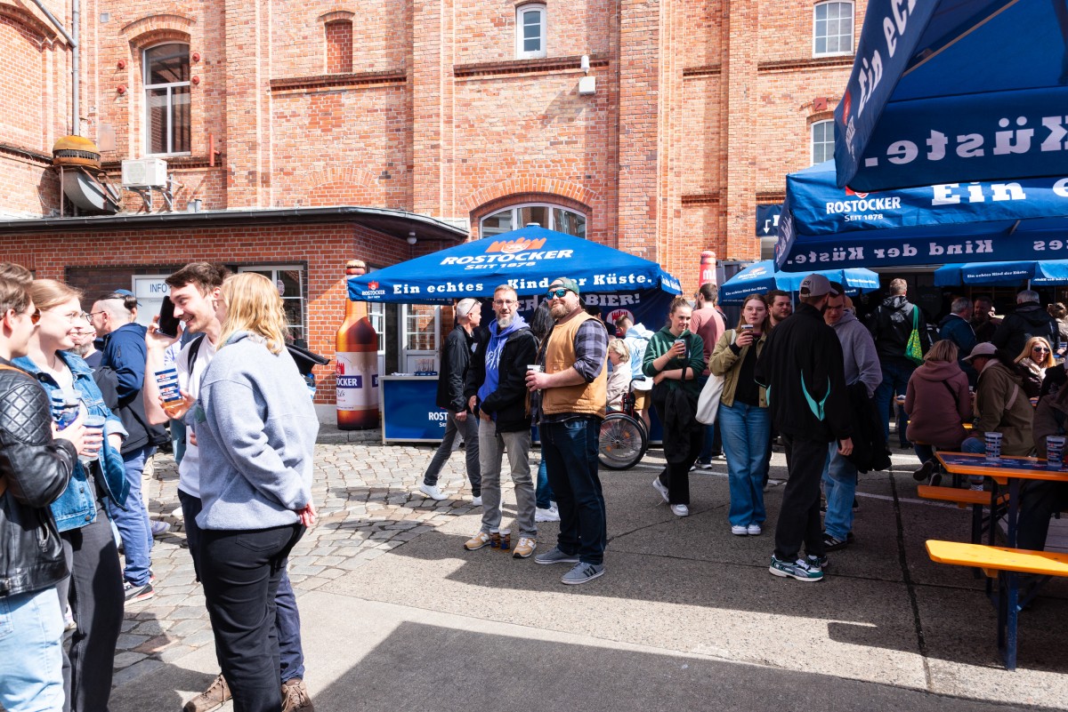 Viele Menschen feiern im Innenhof der Rostocker Brauerei, im Hintergrund ein rotes Backsteingebäude.